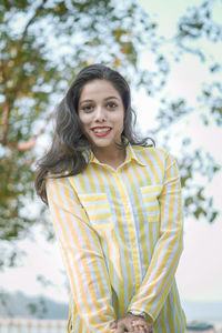 Portrait of smiling young woman standing against trees