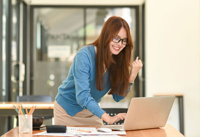 Portrait of young woman using laptop while sitting in office