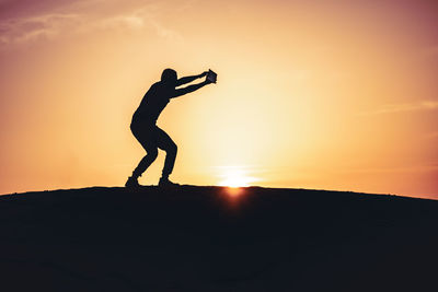 Silhouette man standing against orange sky during sunset