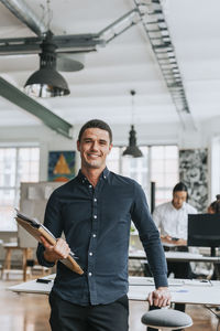 Portrait of smiling businessman with files standing at office