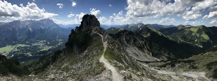 Panoramic view of narrow ridge across alpine mountains against blue and white sky