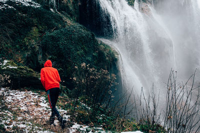 Rear view of person standing by waterfall