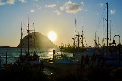 Boats moored in harbor at sunset