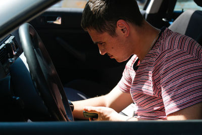 Serious successful caucasian young man sitting in car. 20s guy looking down from window. silver grey 