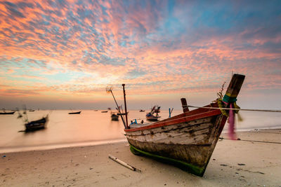 Fishing boats moored on sea against sky during sunset