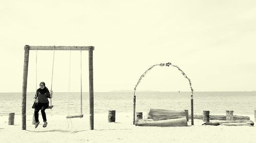 Woman swinging on beach against clear sky