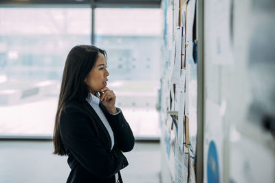 Thoughtful businesswoman examining bulletin board at office