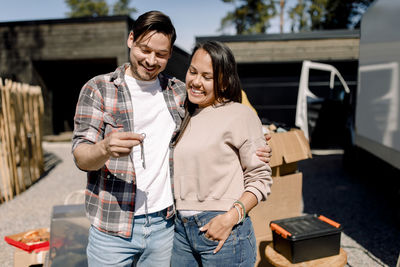 Smiling couple looking at key of new house while standing outside new house