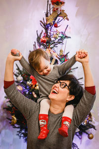 Mother playing with her baby against christmas tree 