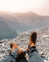 Low section of man relaxing on mountain against sky