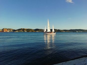 Sailboat sailing on sea against clear blue sky