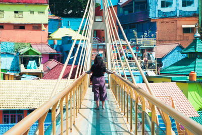 Rear view of woman standing on railing against buildings in city