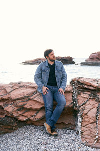 Young man standing on rock against sea