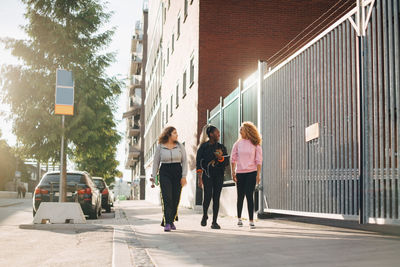 Full length of friends talking while walking on sidewalk in city