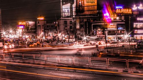 Light trails on road by illuminated buildings in city at night