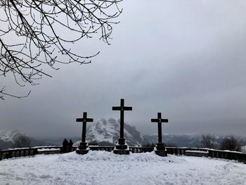 View of cross on snow covered landscape against sky