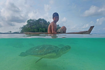 Shirtless boy on boat with turtle swimming in sea