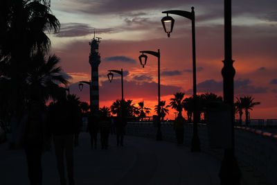 Silhouette people on street against sky during sunset