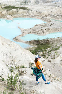 Side view of young woman in cap against  background of blue water of sand clay quarry , landscape