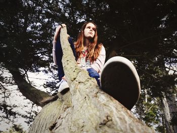 Low angle portrait of young woman sitting on tree trunk