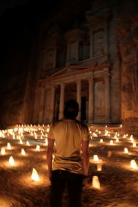 Rear view of man standing against illuminated building at night