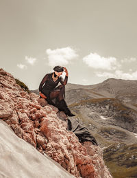 A stylish woman in a black dress sitting on the edge of mountains against the winter sky