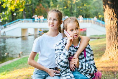 Two girls with push-button phones relax in a summer park