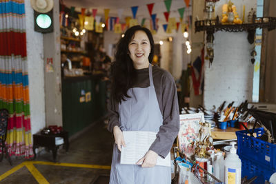 Portrait of smiling female owner holding menu card while standing at restaurant