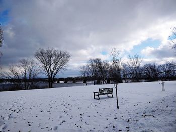 Bare trees on snow covered field against sky