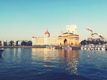 View of buildings by river against clear sky