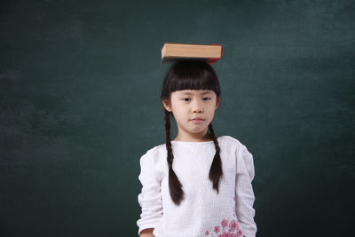 Girl with book on head standing by blackboard