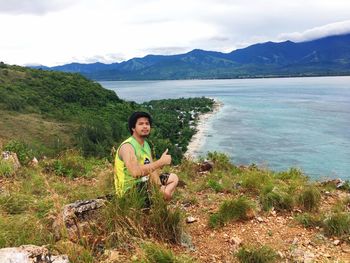 Portrait of man sitting on cliff by sea against sky