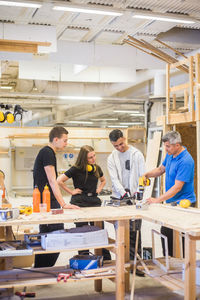 Male carpenter explaining power drill to trainees at workbench during training