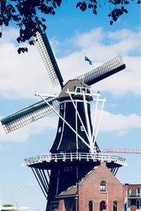 Low angle view of traditional windmill by building against sky