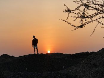 Man standing on rock against sky during sunset