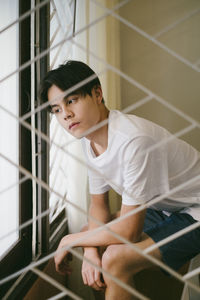 Portrait of young man sitting against wall