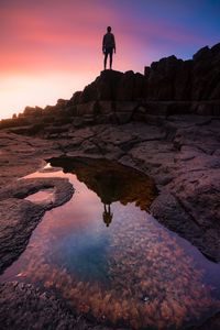 Silhouette man on rock reflecting in water man at sunset