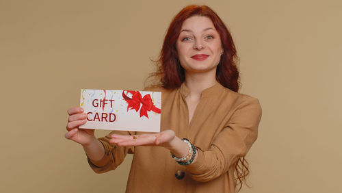 Portrait of young woman holding paper against white background