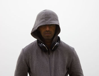 Portrait of young man wearing hood while standing against white background