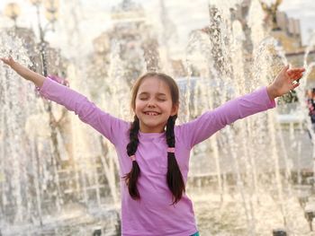 Happy girl with arms outstretched standing against fountain
