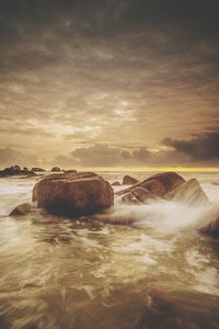 Rocks in sea against sky during sunset