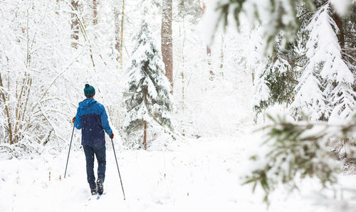 Skier in windbreaker and hat with pompom with ski poles in his hands with his back 