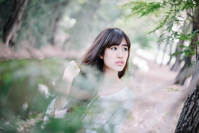 Portrait of young woman standing against trees