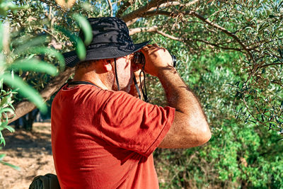 Rear view of tourist man looking through binoculars at the mountains view. hiking, unity with nature