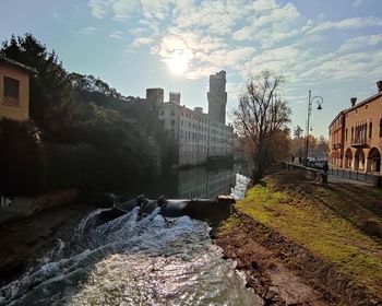Buildings by river in city against sky