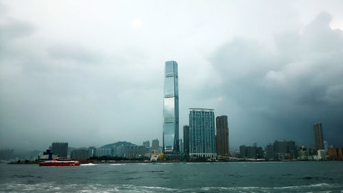 View of city at waterfront against cloudy sky