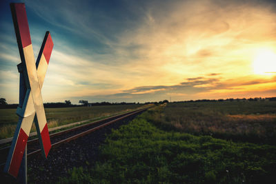 Railroad track amidst field against sky during sunset