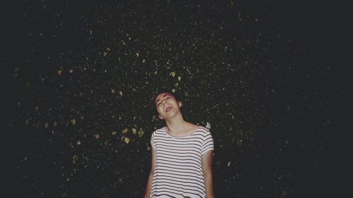 Cheerful young woman standing against plants at night