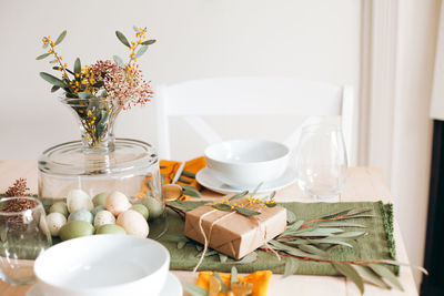 Close-up of glass vase with easter eggs and eucalyptus leaves on dinner table