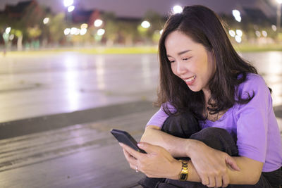 Teenage girl looking away while sitting on illuminated mobile phone